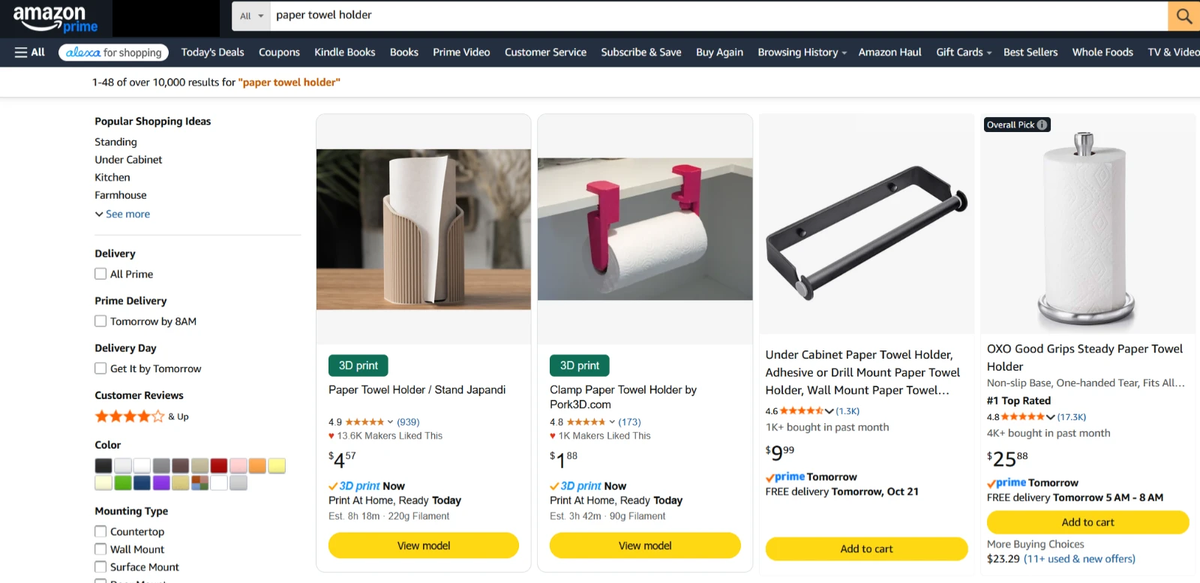 Amazon search results for paper towel holder with two Print The Cart 3D print cards shown first, at $4.57 and $1.88, next to store-bought holders at $9.99 and $25.88.